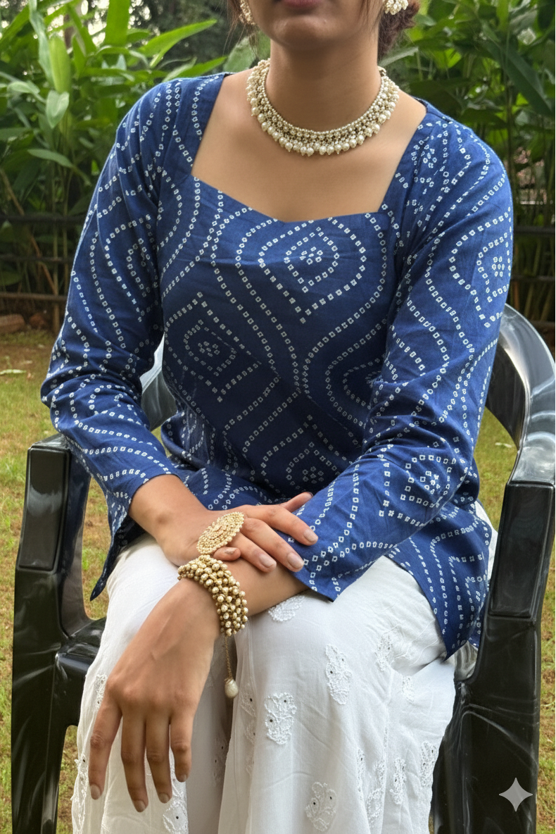 Woman wearing a blue patterned top and white pants sitting outdoors.