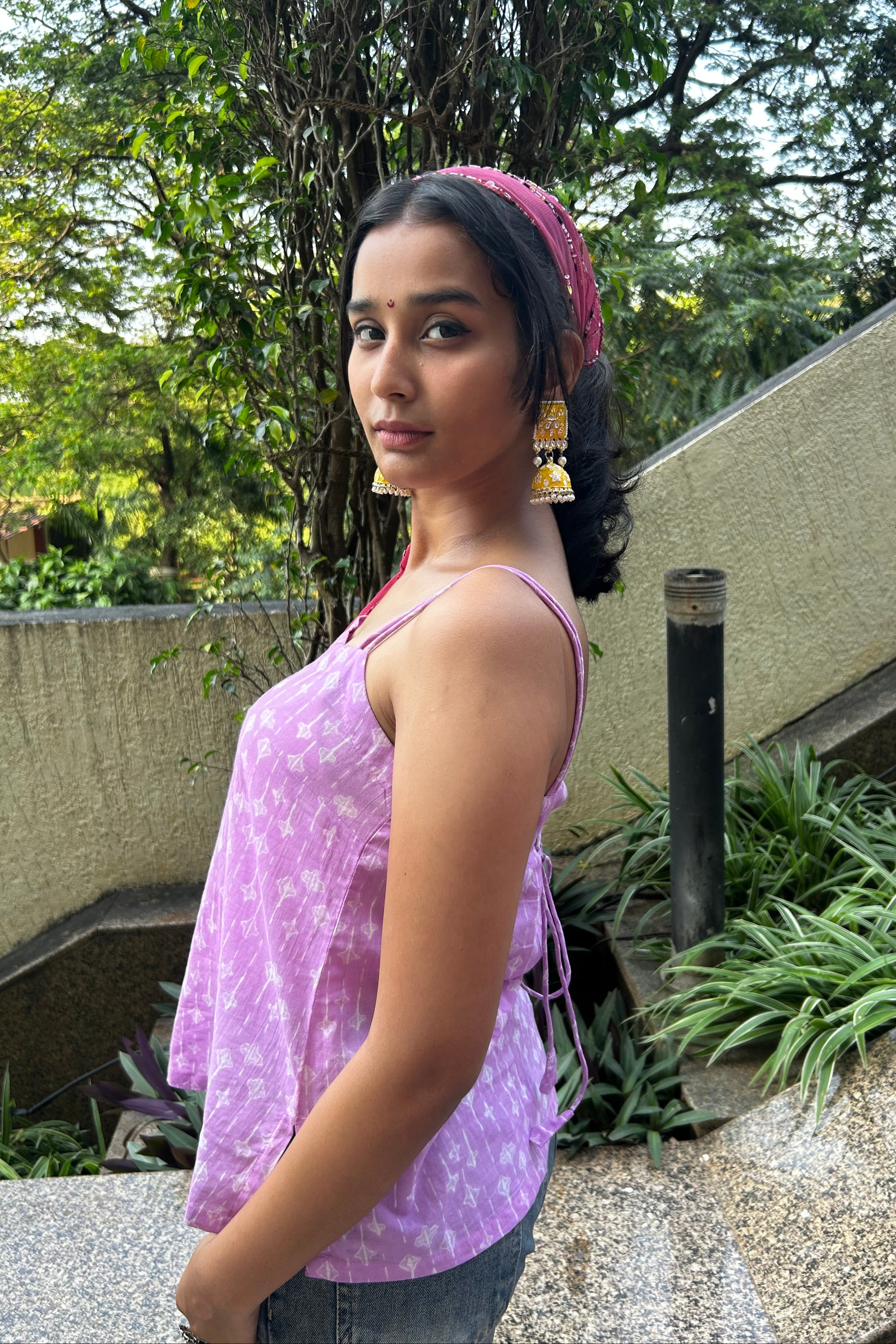 Woman wearing a purple top outdoors with greenery in the background