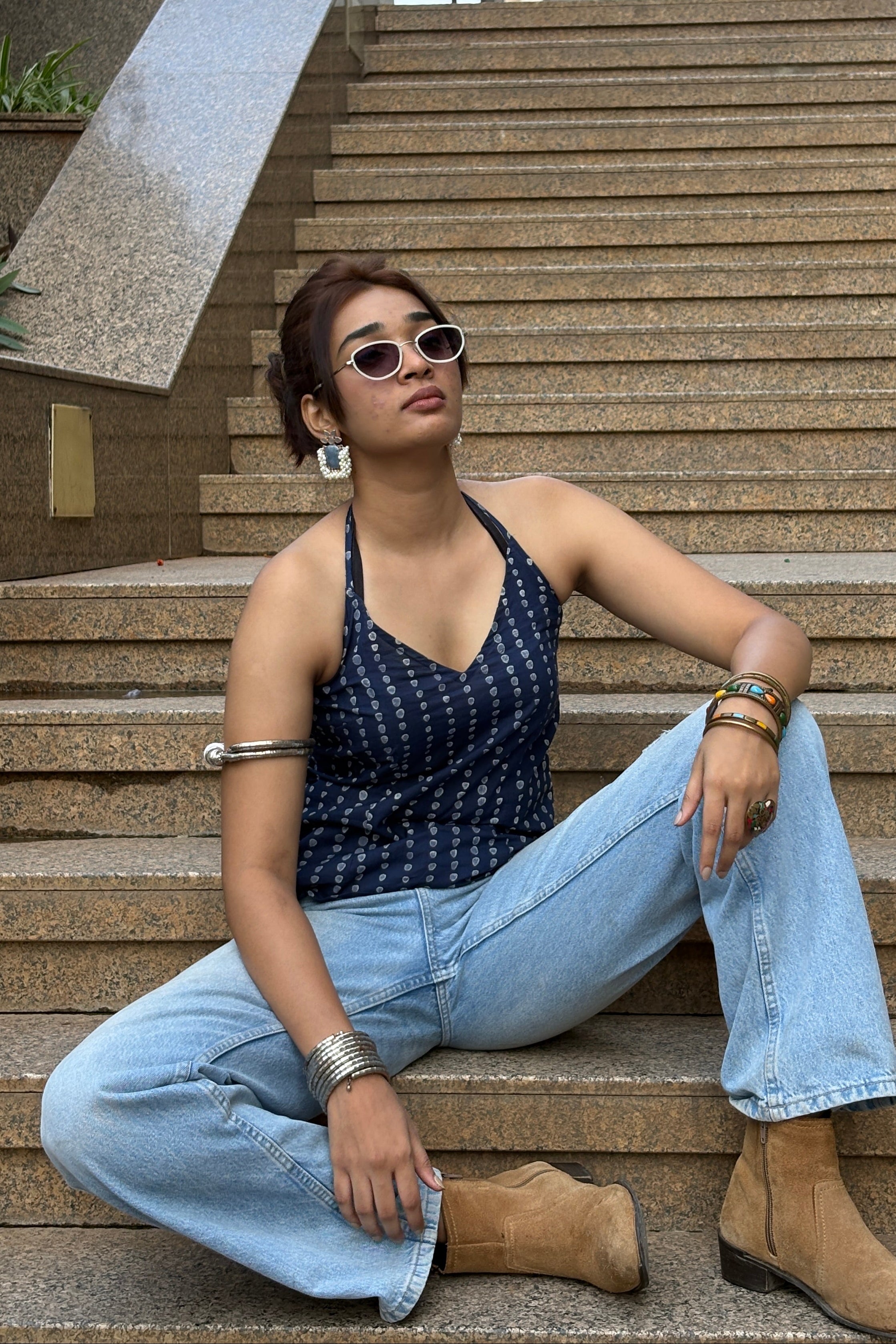 Person sitting on a staircase wearing sunglasses and a blue dress.