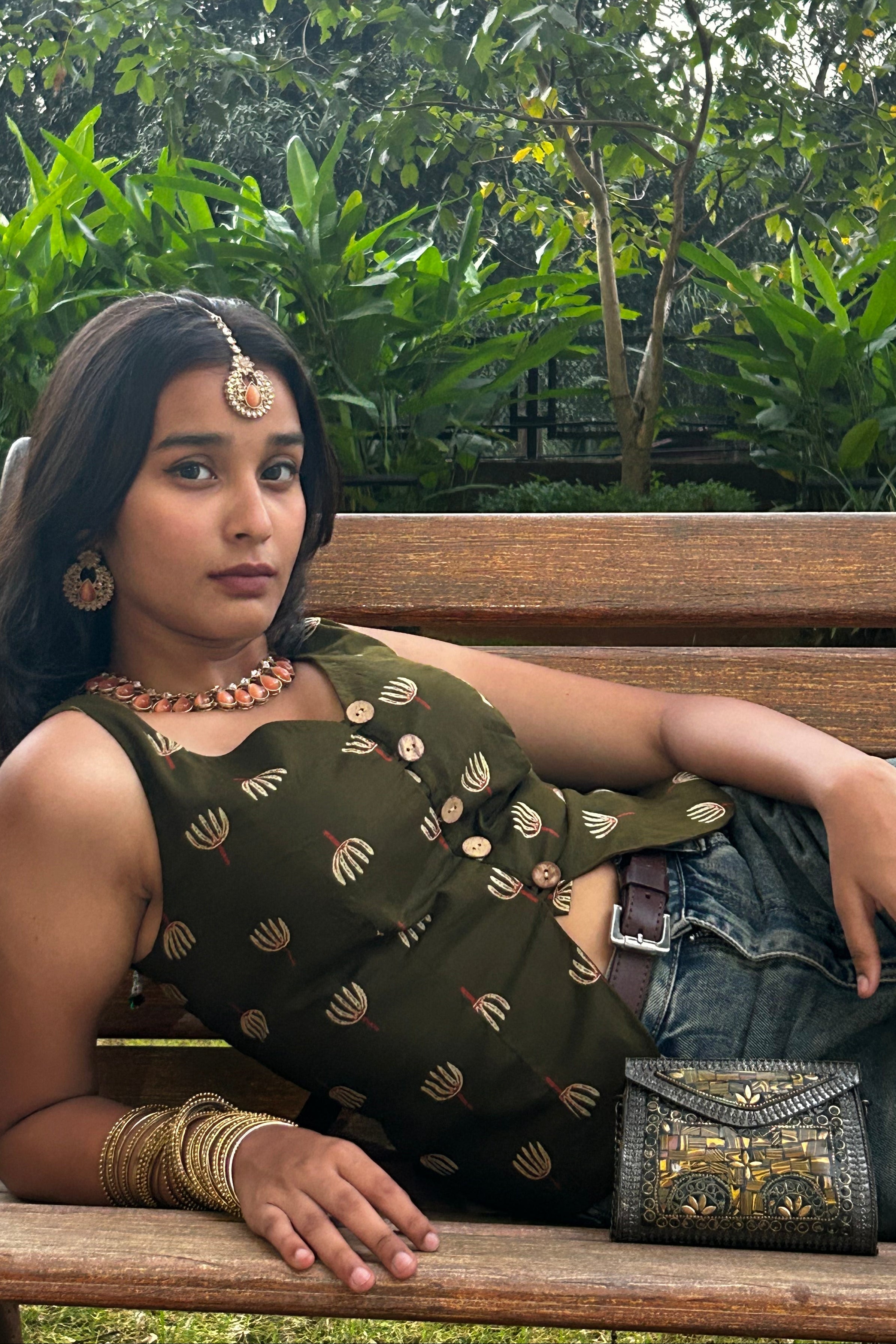 Woman in traditional attire sitting on a bench with greenery in the background