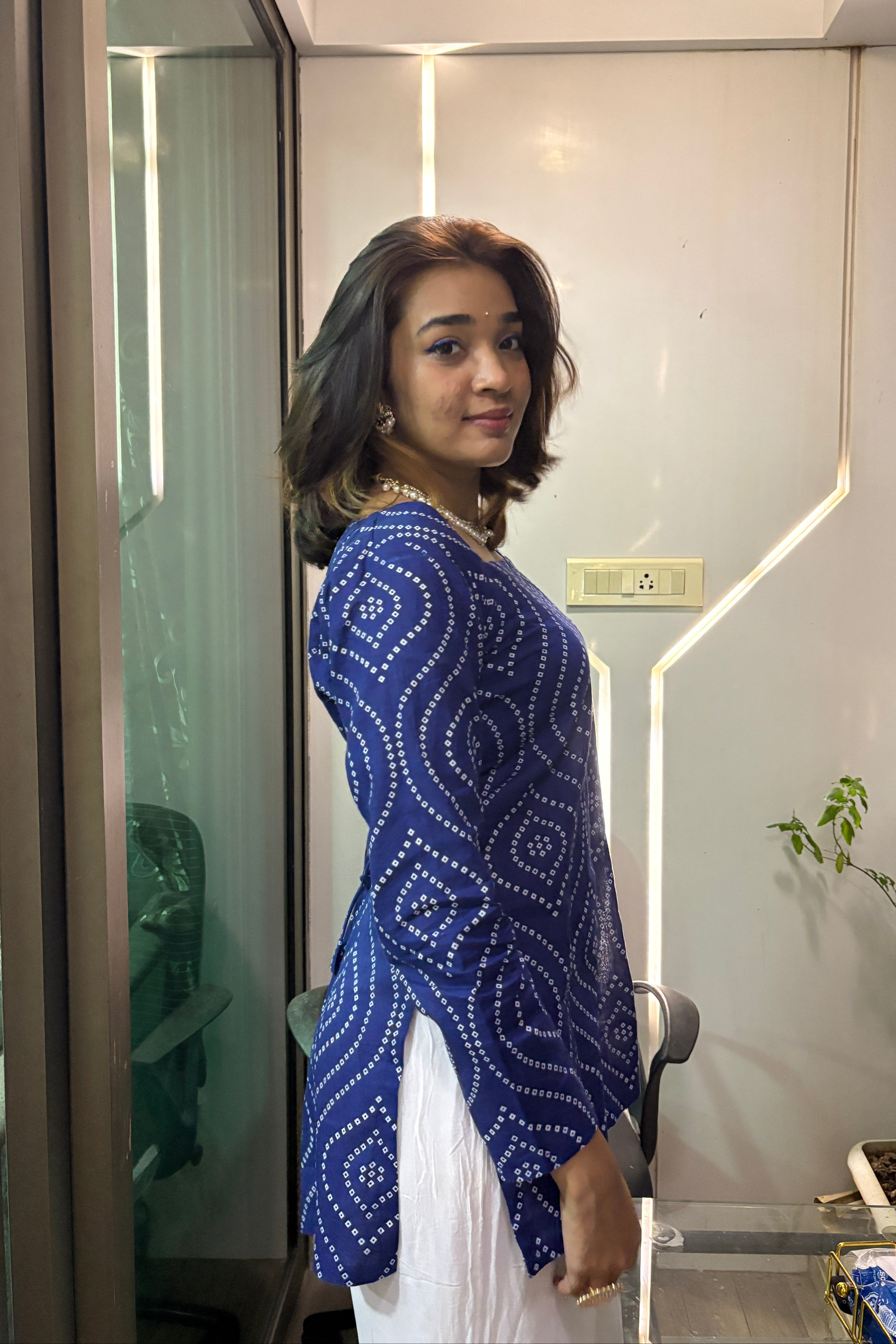 Person wearing a blue patterned top in an indoor setting with a mirror reflection.