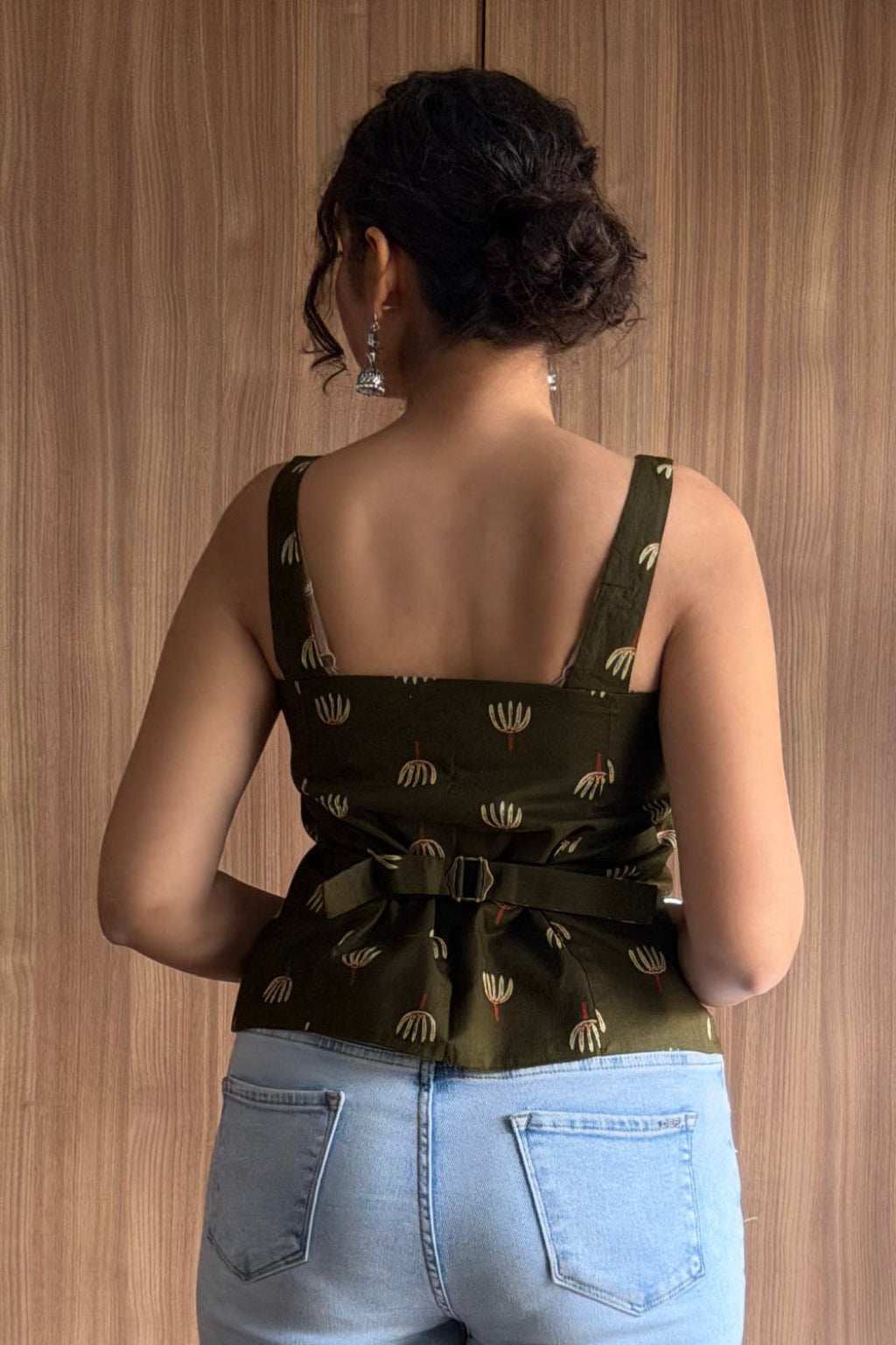 Person wearing a green patterned top and light blue jeans standing in front of a wooden wardrobe.