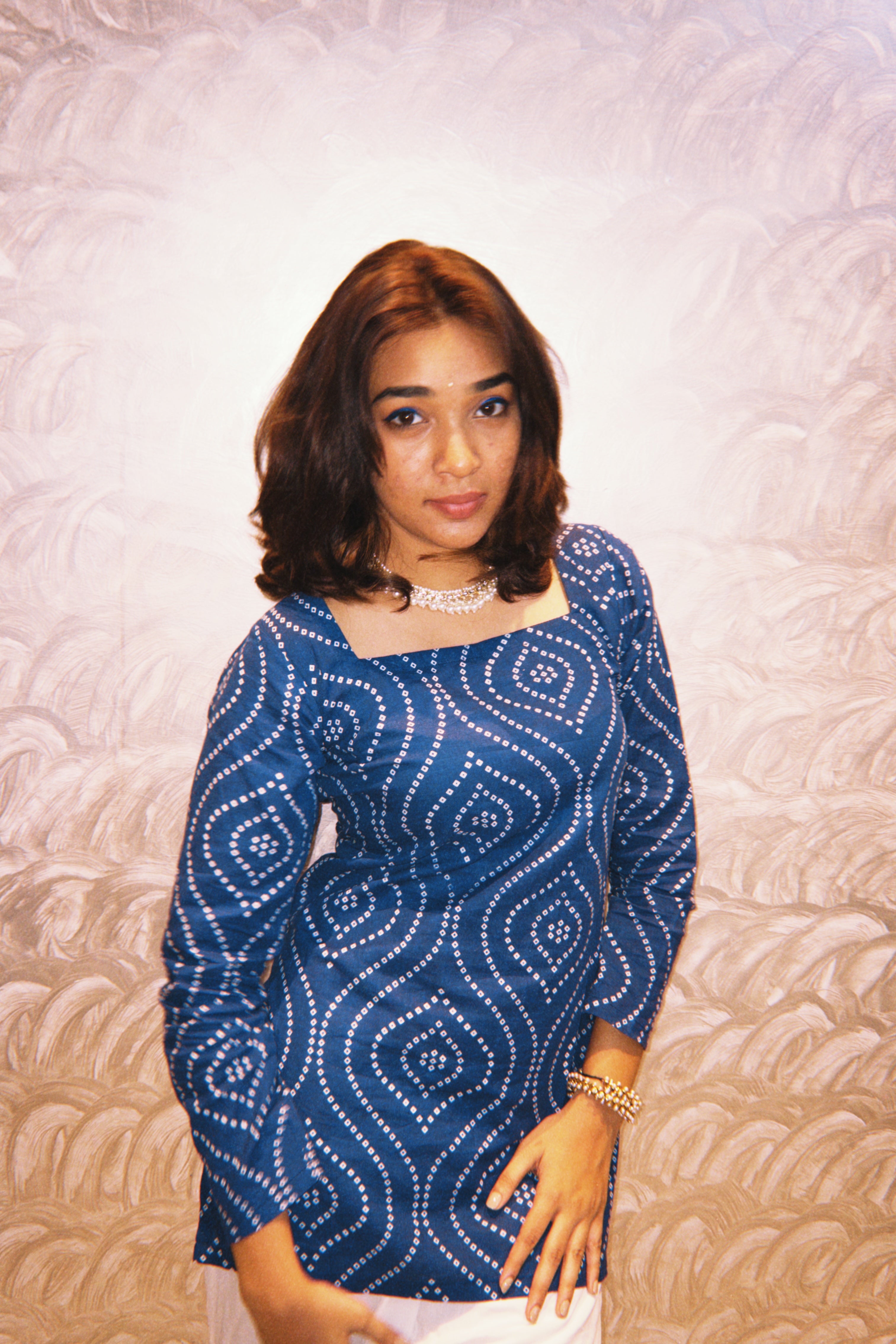 Woman wearing a blue patterned dress against a textured wall.